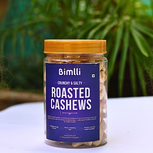 Jar of Bimlli Roasted Cashews with a blue label on a white surface with green foliage in the background