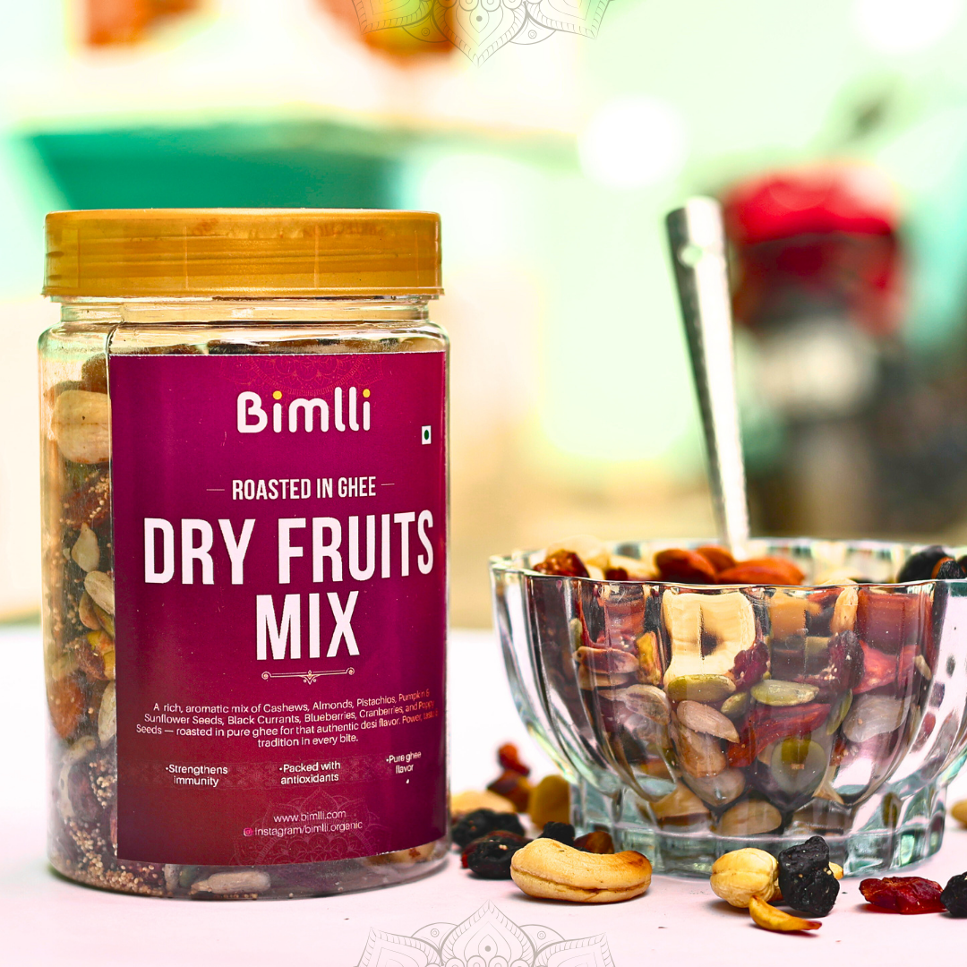 Jar of Bimlli Dry Fruits Mix with a bowl of mixed nuts and fruits on a blurred background