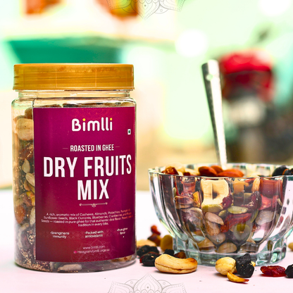 Jar of Bimlli Dry Fruits Mix with a bowl of mixed nuts and fruits on a blurred background