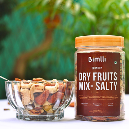 Jar of Bimlli Crunchy Dry Fruits Mix with a bowl of mixed nuts on a blurred green background