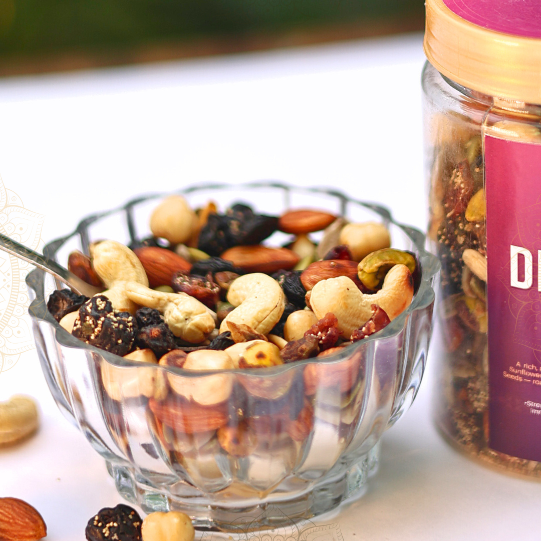 Glass bowl filled with a mix of nuts and dried fruits next to a jar labeled Bimlli Roasted Dry Fruits Mix (Ghee)